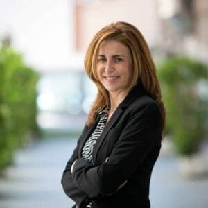 Portrait photo of white woman in suit against background of greenery.